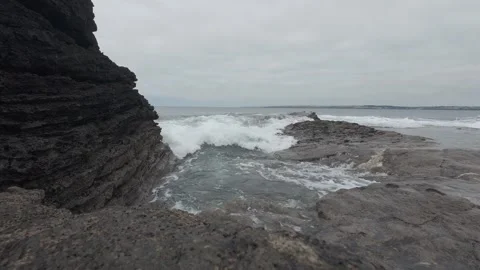 Rough ocean waves breaking against dark cliff rocks on coastline Stock Footage 340457916