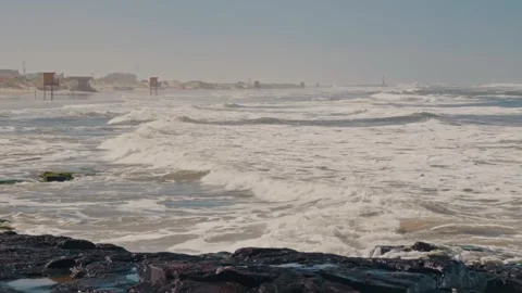 Rough Ocean Waves Crashing on a Rocky Shoreline with Distant Beach and Stock Footage 341322381