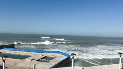 Rough ocean waves crashing on the shore next to an empty seaside swimming pool Stock Footage 339649638