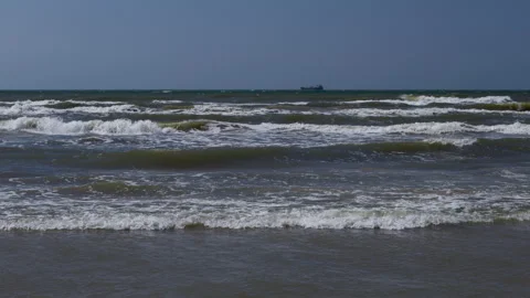 Rough ocean waves rolling toward shore with distant cargo ship on horizon under Stock Footage 346558962