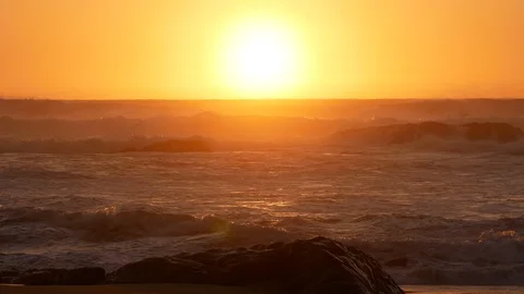 Rough sea on the ocean at sunset with sun center frame and rock in foreground Stock Footage 103186784