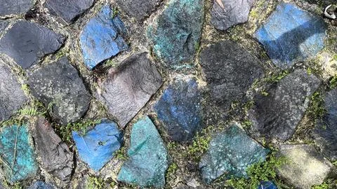 Rough stone wall featuring irregular dark stones with blue and green painted Foto stock