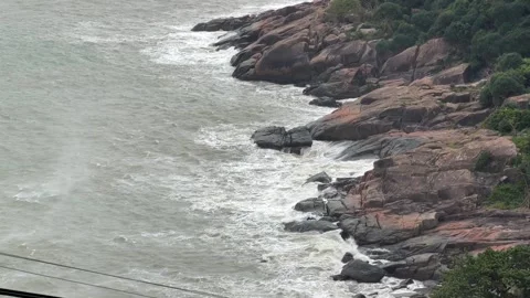 Rough surf crashes along uneven coastal rocks forming swirling white foam as Stock Footage 323981141