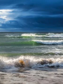 Rough surf rolling in under dark, heavy storm clouds Stock Photos
