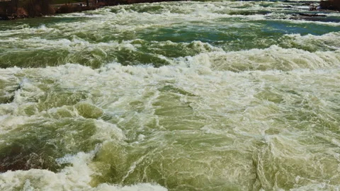 Rough water flows swiftly through a river in the early afternoon under a clear Stock Footage 334158155