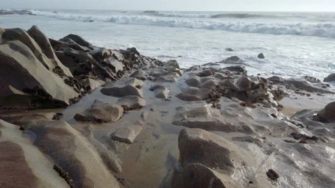 Rough white waves on ocean with sandstone rocks in foreground, slow motion Stock Footage 194201169