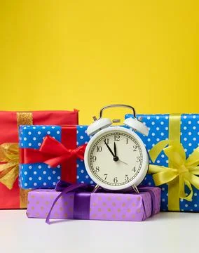 Round alarm clock and a stack of gift boxes tied with a ribbon on a yellow ba Foto stock