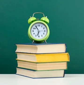 Round alarm clock and stack of books on empty chalk green board background Stock Photos