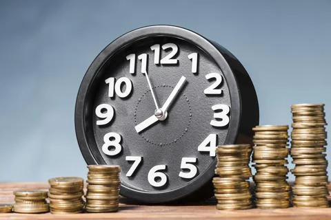 Round alarm clock with stack increasing coins against blue background. High Stockfoto's