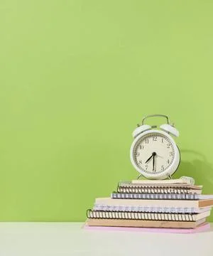 Round alarm clock stands on a stack of notebooks, green background. Round ... Stock-Fotos