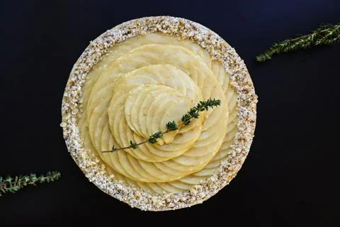 Round apple tart with three thyme sprigs on black font top view Stock Photos