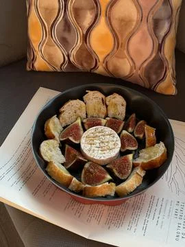 Round baking pan with figs, bread slices, and cheese placed on a newspaper Stock Photos