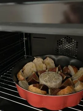 Round baking pan in the oven with bread, figs, and a wheel of cheese Foto stock