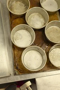 Round baking pans arranged on worn sheet pan in busy commercial bakery kitchen Stock Photos