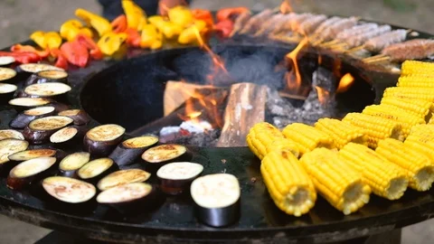 Round barbecue grill with open fire inside. Meals for summer picnic are being Stock Footage 114709020