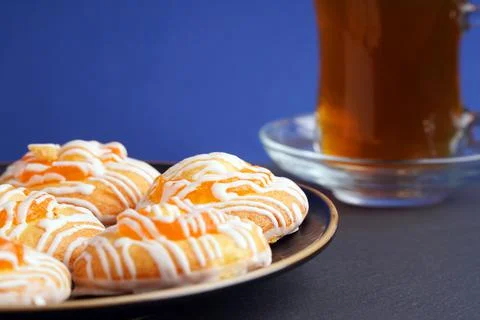 Round biscuits with orange jam on a plate next to a glass of tea on a blue ba Stock Photos