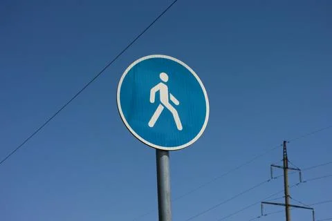 A round blue pedestrian path traffic sign on a metal pole against a blue sky Photos