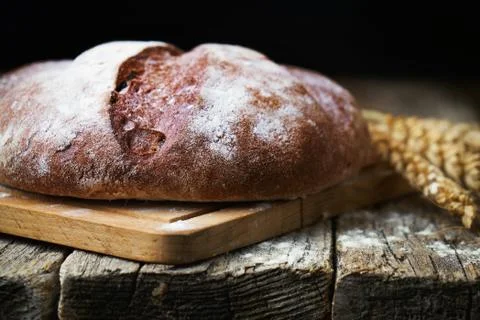 Round bread and wheat ears on the old wooden table Foto stock