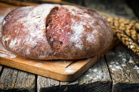 Round bread and wheat ears on the old wooden table Stock Photos