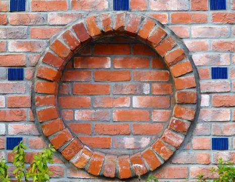 Round brick frame in wall, with ceramic blue tile highlights. Stock Photos