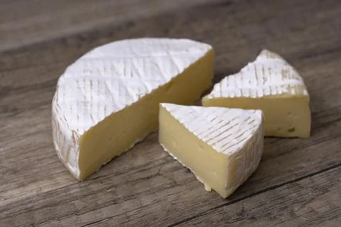 Round Brie cheese with a section cut out over wooden background. Stock Photos