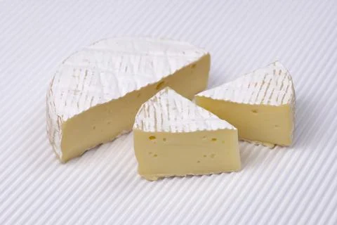 Round Brie cheese with a sections cut out over white corrugated background. Stock Photos