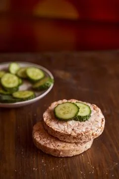 Round buckwheat bread on which are two fresh cucumbers on a brown background Stock Photos