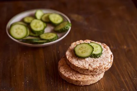 Round buckwheat bread on which are two fresh cucumbers on a brown background Stock Photos