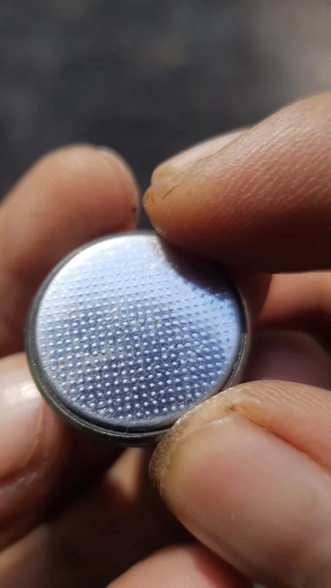 Round button cell battery, shiny metallic coin cell held in fingers, vertic.. Stock Footage 342625888