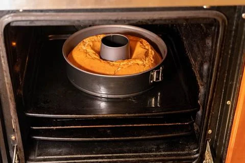 Round cake baking in a circular mold inside an oven Stock Photos
