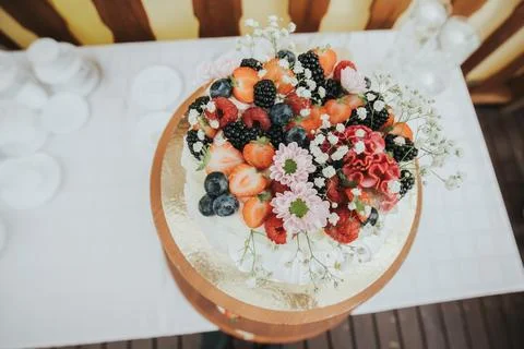 Round cake topped with assorted fresh fruits and flowers, displayed on a wo.. Foto stock