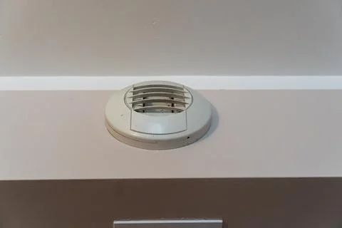 Round ceiling air vent mounted on wall near cornice in residential interior, Stock Photos
