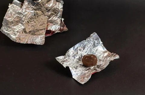 Round chocolate candy and empty wrappers on a black background. Crumpled silv Stock Photos