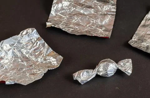 Round chocolate candy and empty wrappers on a black background. A delicious c Stock Photos