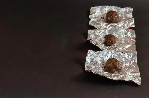 Round chocolates in unwrapped silver wrapper on a black background. Crumpled  Stock Photos