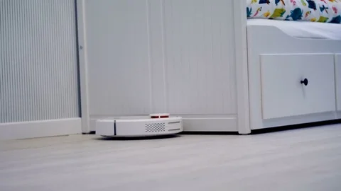 A round cleaning robot slowly moves along a bedroom wall. Stock Footage 81117225