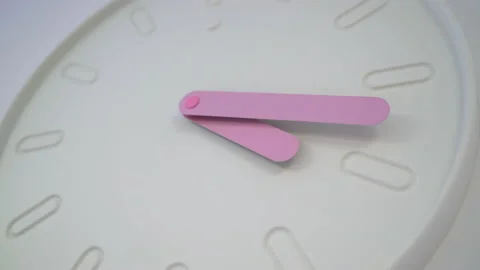A round clock hangs on the wall. Pink hands show the time - hours and minutes. 動画素材 235382795