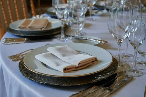 A round dining table with a white tablecloth and cloth napkins is prepared for a Stock Photos