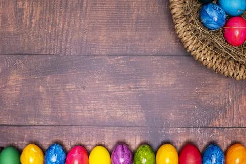 Round Easter basket with colorful Easter eggs on brown wooden tabletop Stock Photos