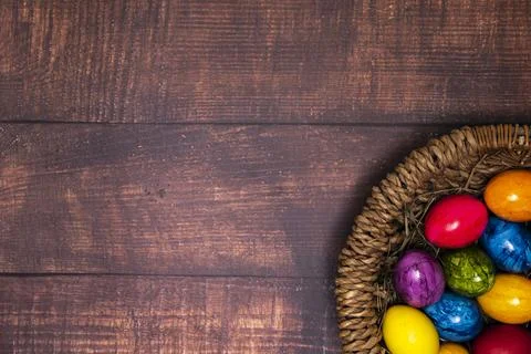 Round Easter basket with colorful Easter eggs on brown wooden tabletop, tab.. Stock Photos