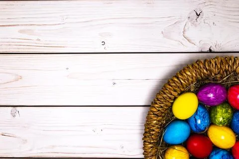Round Easter basket with colorful Easter eggs on white wooden tabletop Stock Photos