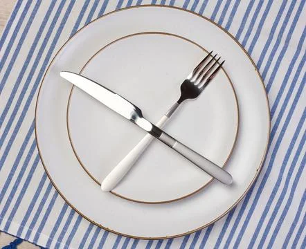 Round empty white ceramic plate, knife and fork crossed, top view Stock-Fotos