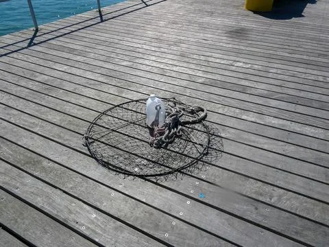 Round fish net attached to a plastic jug of water on a wooden pier near the.. Stock Photos