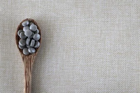 Round gray brown tablets in a spoon on a beige background on the side, top view Stock-Fotos