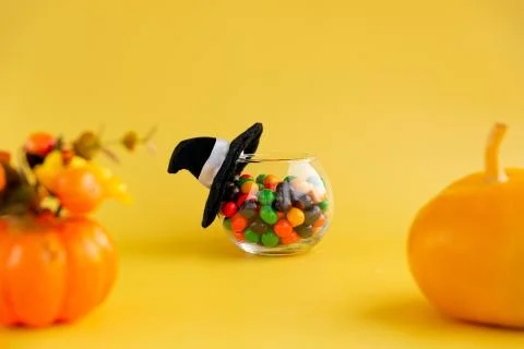 Round jar with multi-colored candies covered with a witch hat and pumpkin on  Stock Photos
