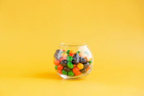 A round jar with multi-colored sweets on a yellow background Stock Photos