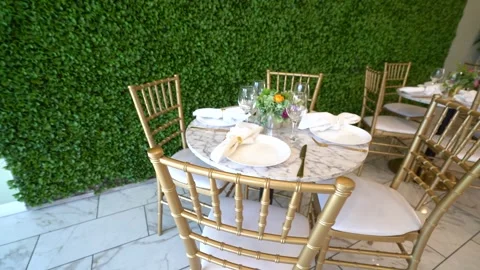 Round marble table with gold chairs beside a green hedge wall Stock Footage 345551145