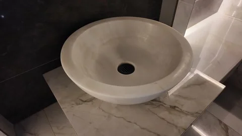 Round matte beige stone sink basin on polished marble countertop in modern Stock Footage 345412493