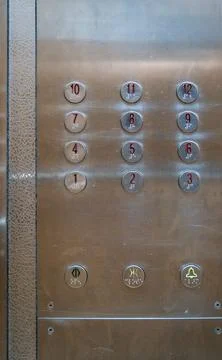 Round metallic buttons on an elevator control panel with signs of wear. Stock Photos