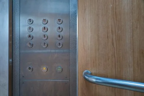 Round metallic buttons on an elevator control panel with wooden interior wall. Stock Photos